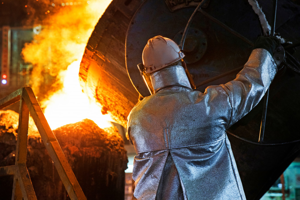Steel mill worker pouring molten metal while wearing protective clothing.